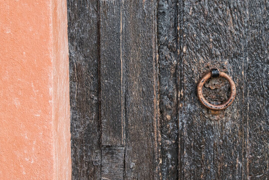 Detail einer alten verwitterten Holzt&uuml;r mit rostigem Eisenring neben terrakottafarbener Wand