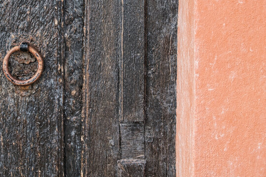Detail einer alten verwitterten Holzt&uuml;r mit rostigem Eisenring neben terrakottafarbener Wand