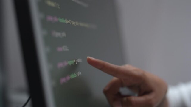 Developer's hand points to a specific line of code displayed on the computer screen during code review.