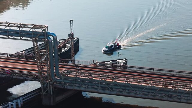 Highangle shot of a small motorboat cruising through an industrial river lock system and under a bridge in Lodz, Poland. Suitable for travel, logistics, and maritime engineering content.