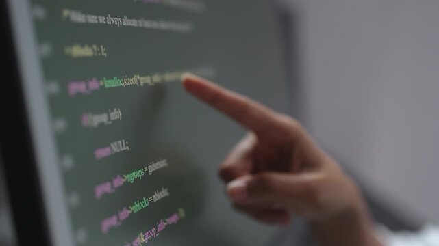 Close up of hand pointing finger at source code on monitor while reviewing and debugging software, checking programming line by line in development work
