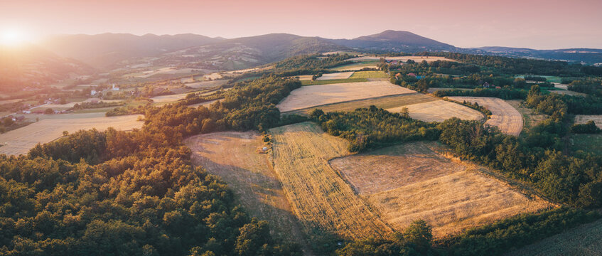 Aerial drone panorama of patchwork farmland and rolling hills at golden hour sunset.