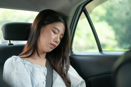 Young Asian woman resting with eyes closed in back seat of a taxi cab car during a relaxing journey.