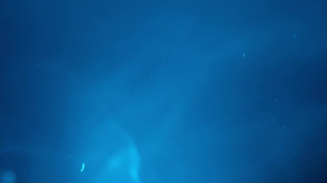 Deep blue abstract background with subtle light rays and soft bokeh creates an atmospheric or underwater concept. This tranquil and serene backdrop offers ample copy space for design, graphic, or