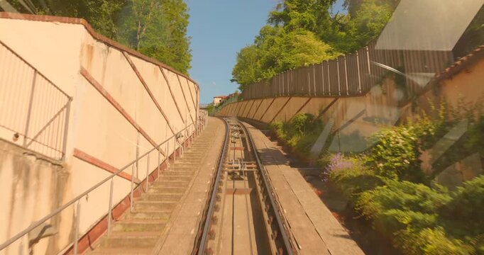 Onboard view of steep Mondovi Funicular railway climbing uphill between retaining walls and green vegetation on a sunny day, Mondovi, Piedmont, Italy