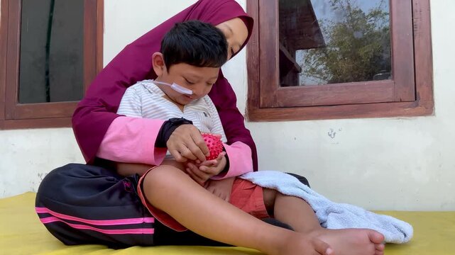 Mother assisting a child with a disability and nasogastric tube during sensory therapy with a textured ball