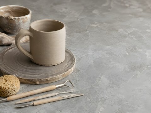 Unfinished clay cup and pottery tools on gray work surface