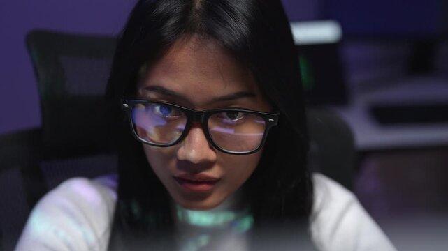 Asian woman programmer with glasses focusing on computer screen debugging errors in AI generated code, reviewing and fixing bugs from artificial intelligence output