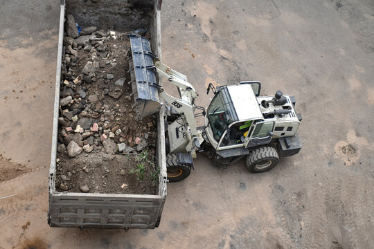 Aerial view of construction site where a front loader is loading soil, rocks, and debris into a dump truck, industrial work, excavation, and earthmoving processes
