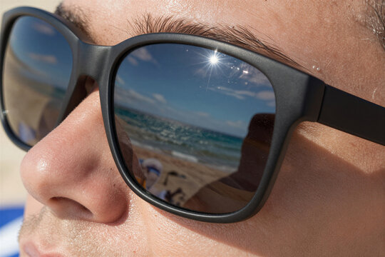 Captures Close Of Individual Wearing Dark Tinted Sunglasses Reflecting Beach Scene Behind Reflection In Right Lens Clear Blue Sky White