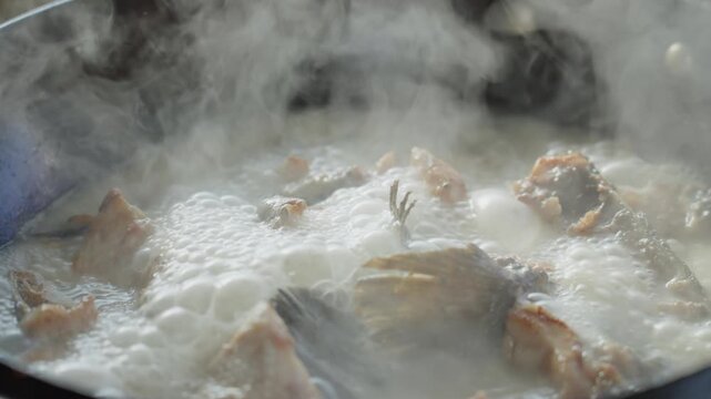 Close-up of fresh fish pieces continuously boiling in thick white soup