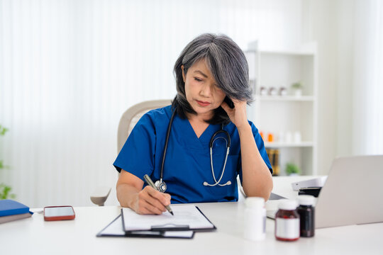 Stressed Female doctor nurse sit by laptop computer while reviewing patient medical charts at the clinic office.