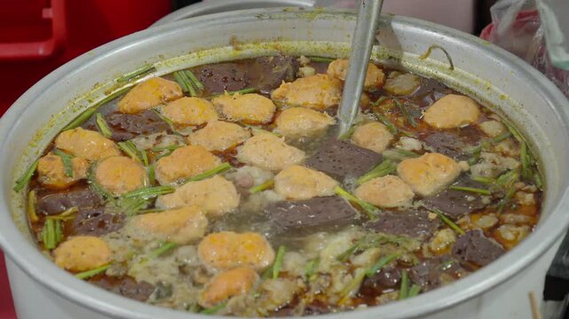 A large pot of broth simmers with orange meatballs, sliced blood sausage and scallions at a Vietnamese food stall in Hue, Vietnam.