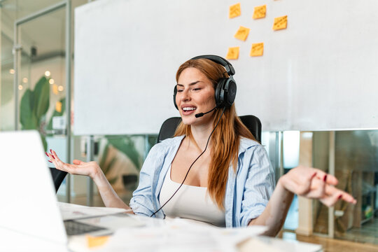 Smiling young businesswoman with vitiligo wearing headset and gesturing while talking on video call in office. Remote work meeting and virtual conference discussion concept in modern workplace setup