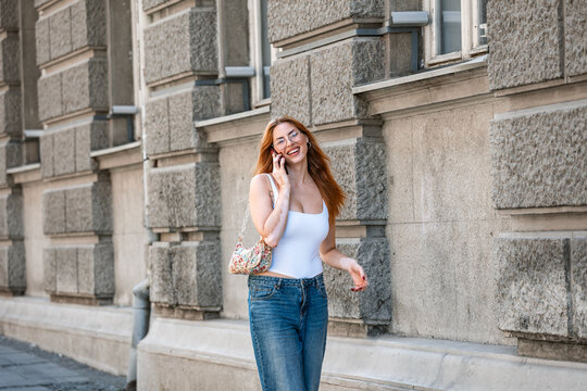 Smiling young woman with vitiligo walking on the city street while talking on her mobile phone. Urban lifestyle communication and wireless technology concept outdoors during a sunny day 