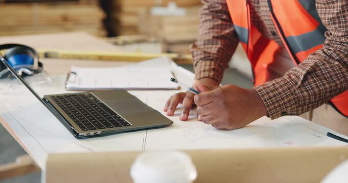 Person, hands or carpenter writing with laptop in warehouse for furniture design or timber project. Carpentry, builder or taking notes with computer or documents for wood production or lumber plan