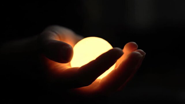 Close-up footage of holding a glowing sphere, holding a warm light sphere in both hands