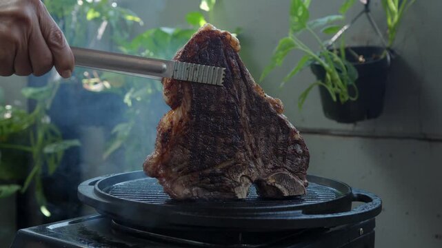 Man grilling a porterhouse steak over cast iron griddle, the smoke is visible through the high-heat sear, suitable for summer grill theme 