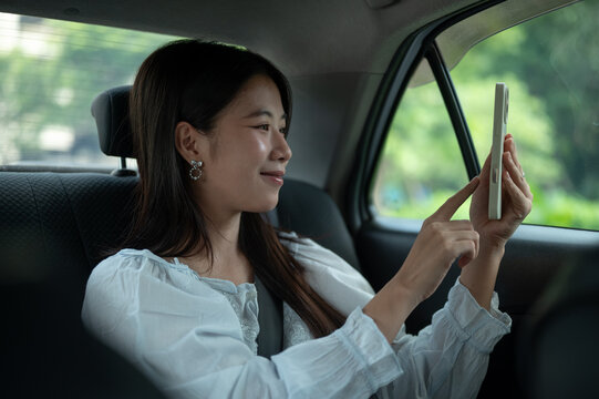 Young Asian woman taking a selfie photo with smartphone while sitting in back seat of a taxi cab car