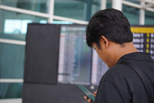 Man checking travel information on a smartphone with a blurred digital flight information board at an airport