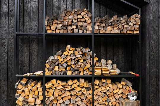 Vertical view of split firewood stacked in compartments on a black metal rack against dark charred timber cladding, creating a warm rustic contrast