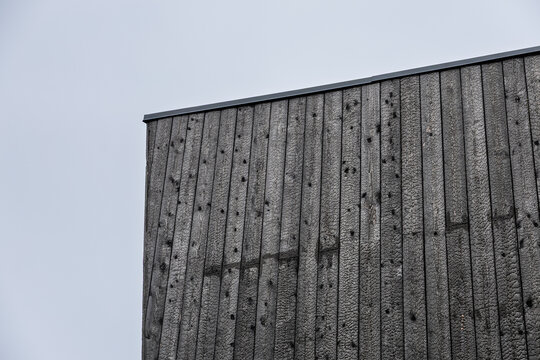 Low-angle detail of a modern facade clad in vertical black Shou Sugi Ban timber boards beneath a pale overcast sky, creating strong contrast and ample copy space