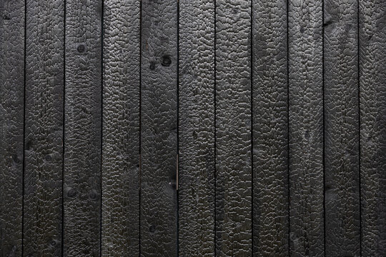 Full-frame texture of vertical black Shou Sugi Ban timber boards with deeply charred grain, knots, narrow seams, and a rugged carbonized surface