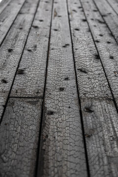 Close perspective view of black Shou Sugi Ban timber boards with cracked carbonized grain, dark knots, seams, and shallow depth of field