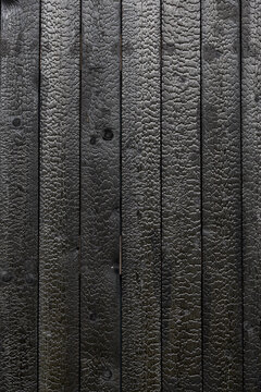 Full-frame texture of vertical black Shou Sugi Ban timber boards with deeply charred grain, knots, narrow seams, and a rugged carbonized surface