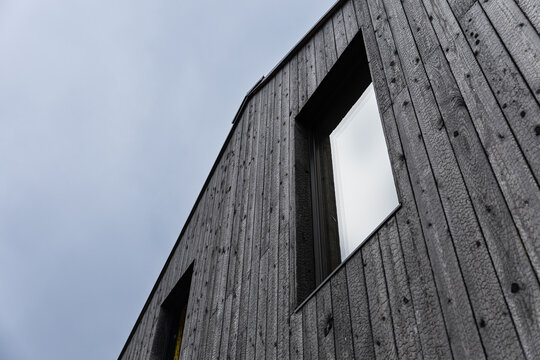 Low-angle view of a modern building clad in black Shou Sugi Ban timber, featuring vertical charred boards, a reflective window, geometric lines, and sky copy space