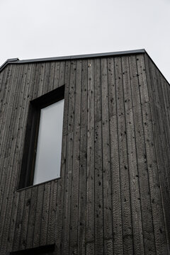 Low-angle view of a modern building clad in black Shou Sugi Ban timber, featuring vertical charred boards, a reflective window, geometric lines, and sky copy space