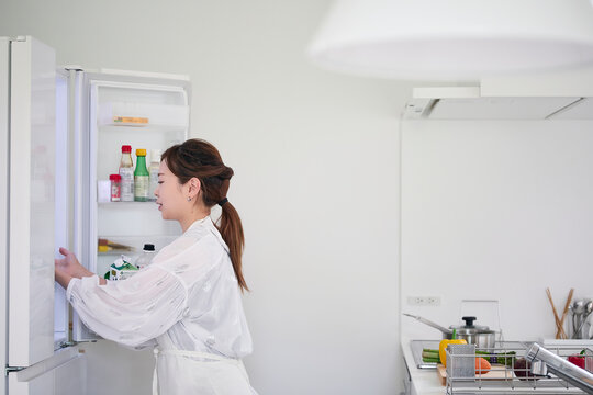冷蔵庫を開けキッチンで料理を作る女性