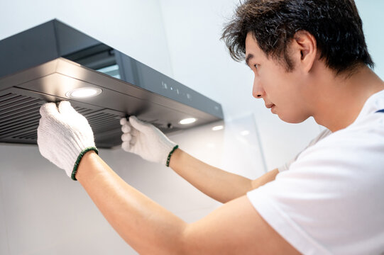 Asian male maintenance worker repairing modern cooker hood in domestic kitchen. Technician man wearing gloves cleaning kitchen range hood filter for clear ventilation. Home appliance service on site
