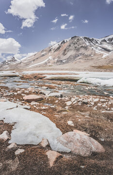 Landscape in the high Pamirs with rocky peaks and a river in a valley with melting snow. Panorama of rocky mountains on a sunny day and glaciers in a river valley