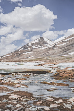 Landscape in the high Pamirs with rocky peaks and a river in a valley with melting snow. Panorama of rocky mountains on a sunny day and glaciers in a river valley