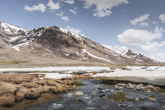 Landscape in the high Pamirs with rocky peaks and a river in a valley with melting snow. Panorama of rocky mountains on a sunny day and glaciers in a river valley