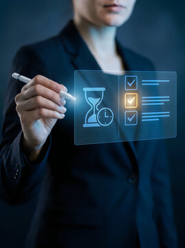 A woman in a business suit using a stylus to interact with a glowing digital interface showing an hourglass timer and a checklist with checkmarks