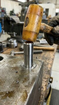 Artisan Uses a Mallet to Carefully Seat a Steel Component into a Heavy Industrial Base within a Professional Machine Shop Environment