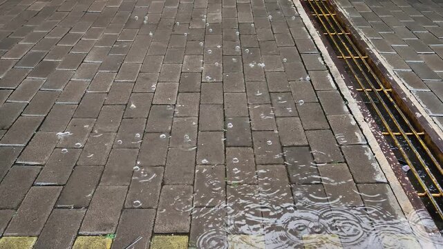 Raindrops splashing in puddle on paved sidewalk near gutter