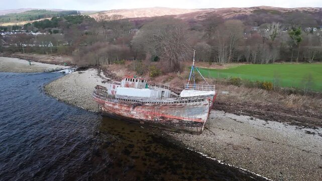 Decaying wooden shipwreck stranded on a shingle beach at Corpach, Scotland.