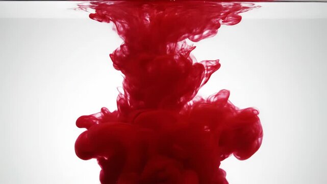 Abstract red ink or paint dissolving and spreading dramatically underwater, forming vibrant plumes and cloud patterns against a stark white background in slow motion.