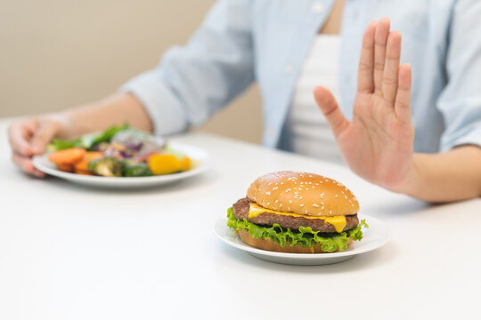 Diet concept, asian young woman hand reject eat burger, hamburger on plate, push out or deny to eat fast, junk food choose green vegetable salad, girl eat low fat for good healthy, getting weight loss