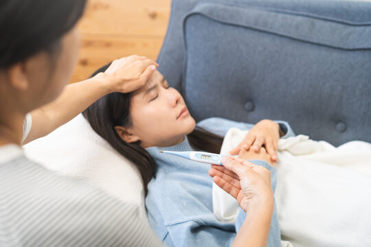 Sick, influenza asian young woman tired have a fever sleep on couch hand holding thermometer for check measure body temperature, illness while rest at home. Health care with disease, pandemic virus.