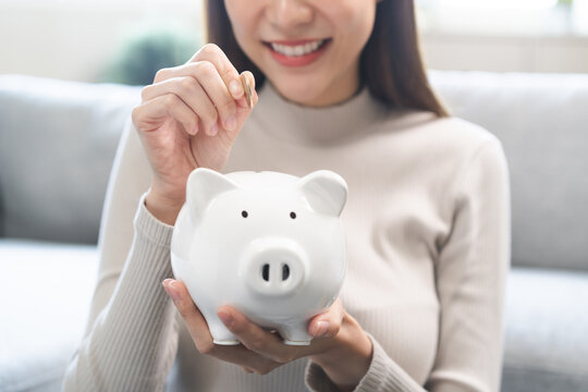 Saving money wealth concept, asian young business woman hand putting coin into piggy for saving cost, cash finance planning to spend enough money on her income for save money, payment tax, investing.