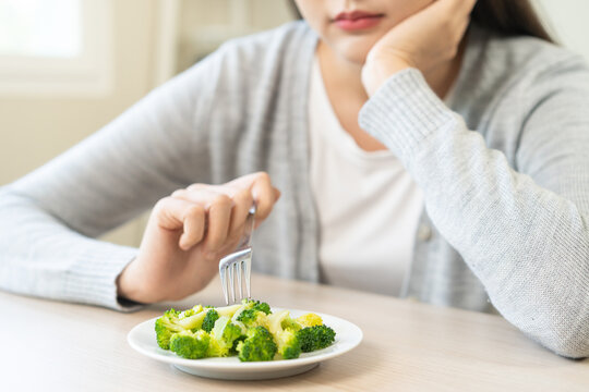 Diet in bored concept, Ketogenic, Low carb, Intermittent Fasting young woman dieting holding fork at broccoli on salad plate tired with eat fresh vegetables. Nutrition clean, healthy food good taste.