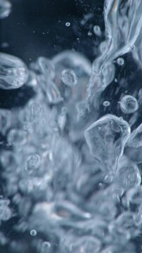 Air Bubbles Rising Underwater. Macro view of clear bubbles swirling upward through dark blue water in slow motion.