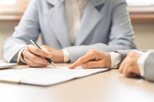 Business people signing contract signature for agreement on papers while customer, partner, coworker holding pen putting signs signature at desk office, one person point to offer letter at desk office