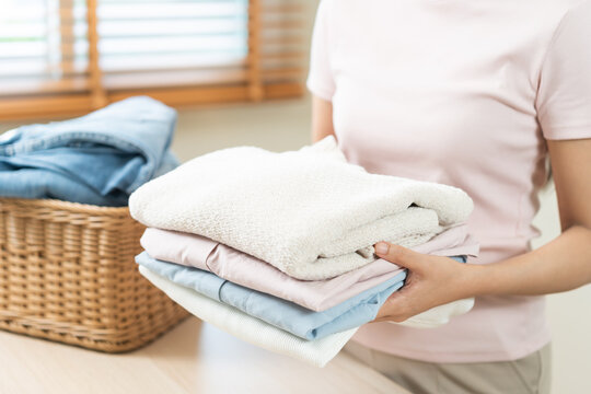 Feel softness, chore of asian young woman, girl housewife hand holding pile clothing from table, stack folding clean clothes after washing, laundry and dry, working at home. Laundry maid in household.