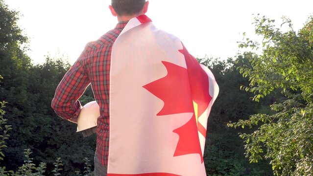 Construction worker holds a white hard hat with a Canadian flag draped over his shoulder. Symbolizes Canadian workers or Labor Day. Concept of pride in construction profession