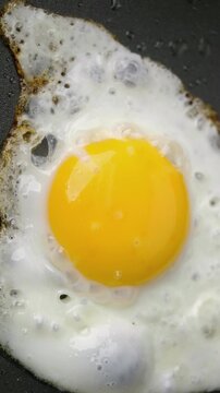 Fried Egg Cooking in Pan. Close-up of a sunny-side-up egg sizzling as the white bubbles and browns. Ideal for breakfast and cooking concepts.